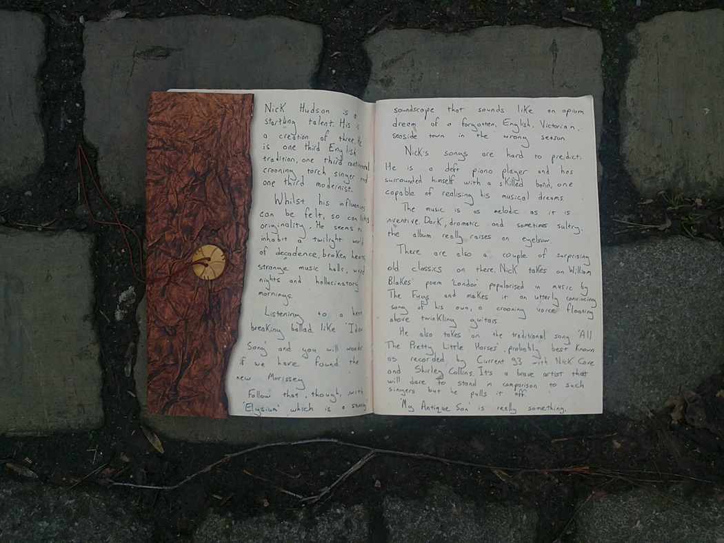 a hand written review of the album My Antique Son by Nick Hudson, written in an odd little journal and photographed on a steep and ancient highway